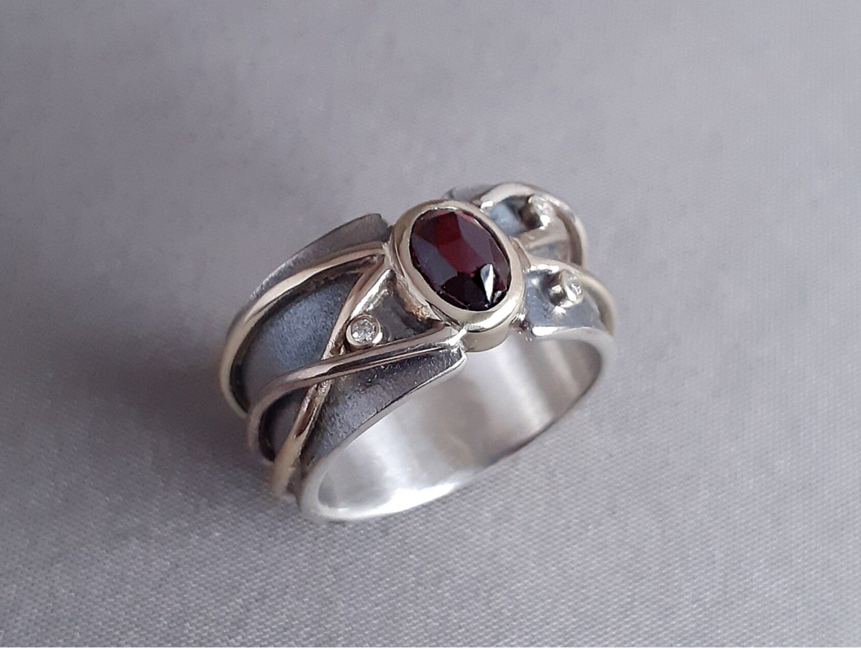 Dit is een handgemaakte ring. De basis is gemaakt van eigen zilver, met daarover draden van eigen geel en witgoud. De granaat en diamantjes zijn ook van de klant zelf. 