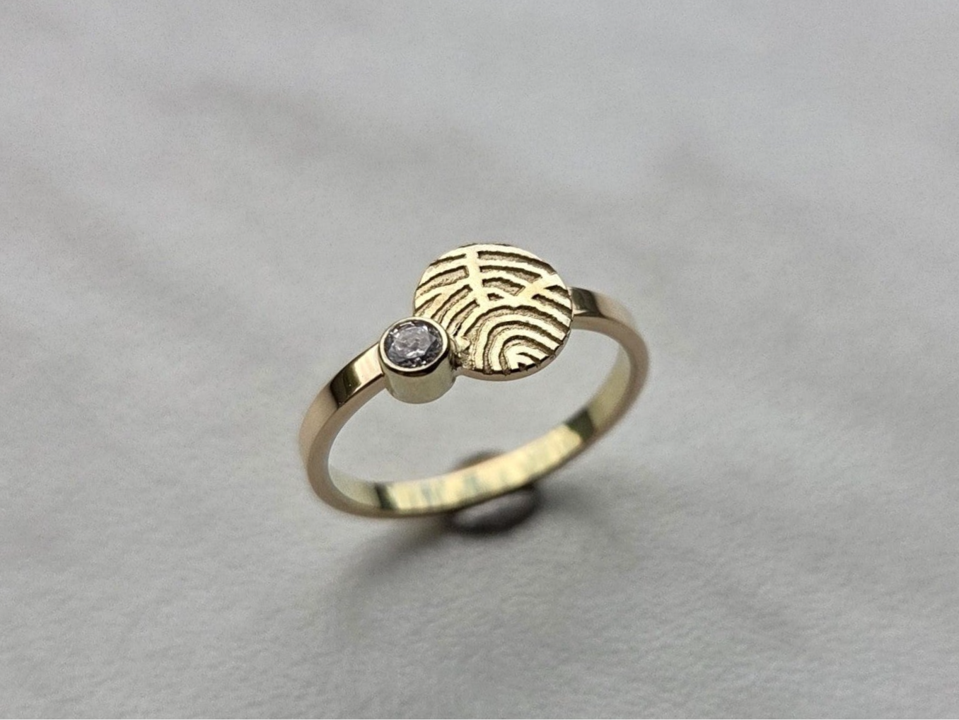 Gouden ring met een vingerafdruk op een rondje en met daarlangs een zirkonia met as onderin het dichte zetkastje.