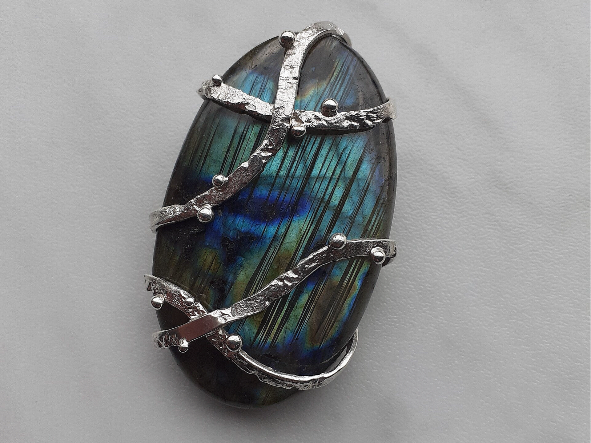 Een zilveren hanger met een grote Labradoriet, gewikkeld in gesmolten draden. 