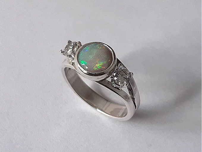 Een zilveren ring met opaal in een zetkast en 2 zirkonia's in een chatonzetting. 