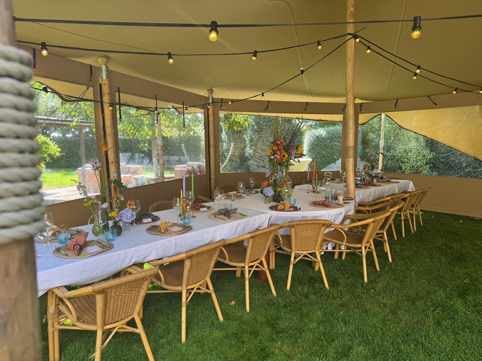 Gedekte dinertafels met rotanstoelen, prikkabelverlichting en transparante zijwanden onder een stretchtent