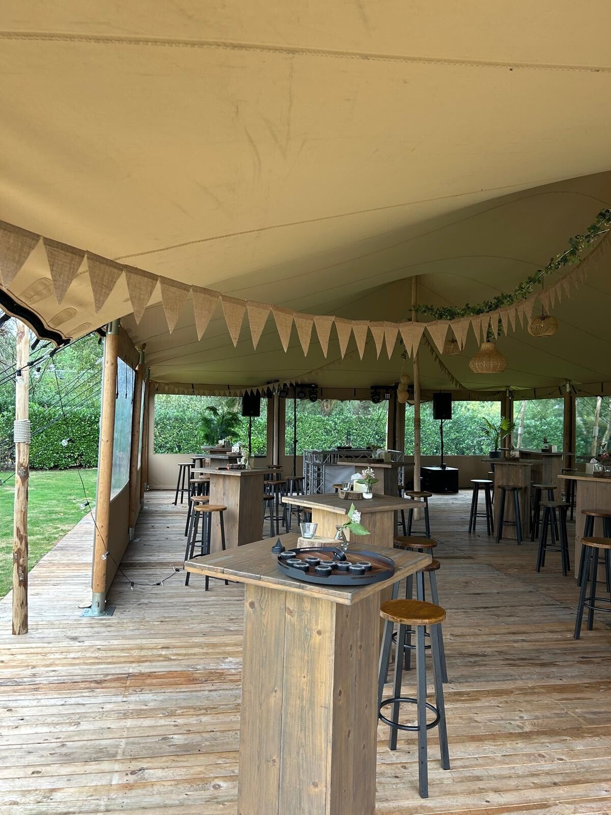 Stretchtent ingericht voor een borrel met houten statafels, barkrukken en een vlondervloer
