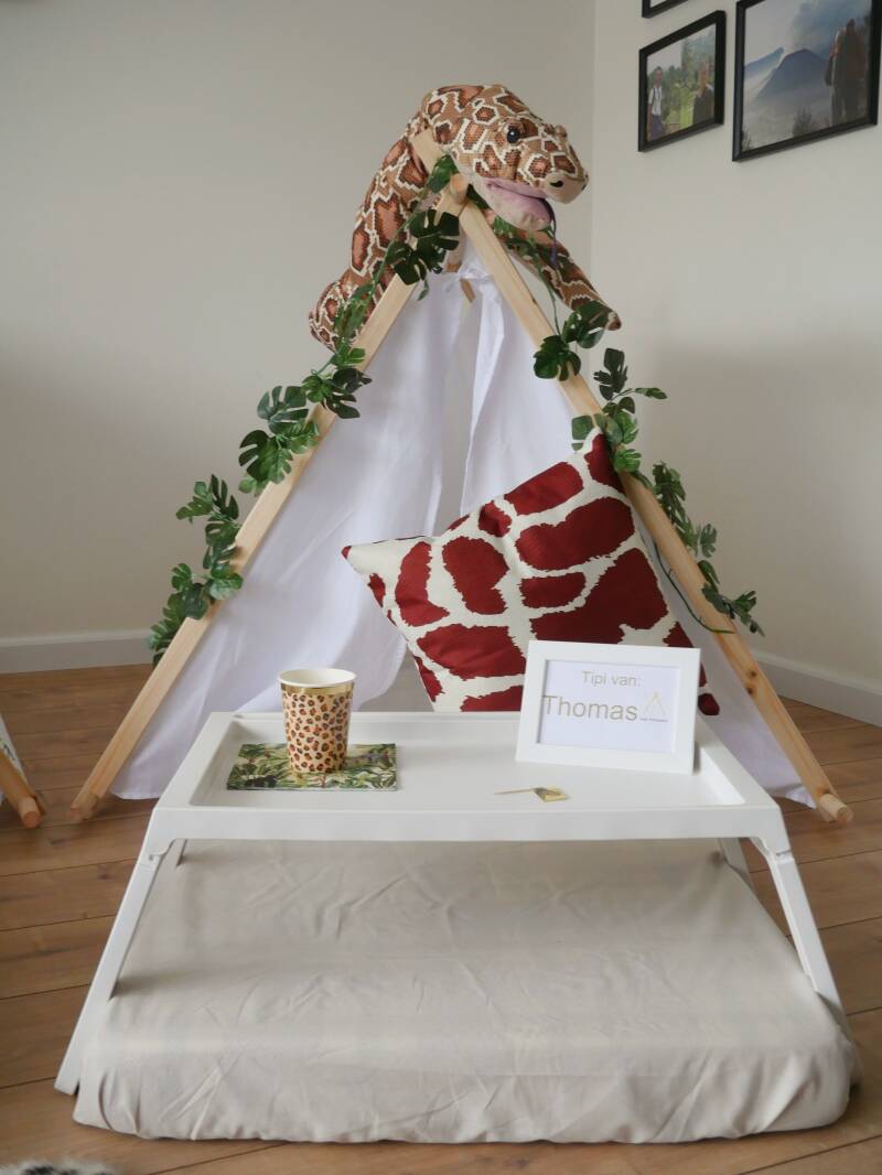 wit tipi tentje ingericht met jungle safari thema voor kinderfeestjes en  slaapfeestjes, met bedtafeltje groene bladeren, slang en dierenprints.