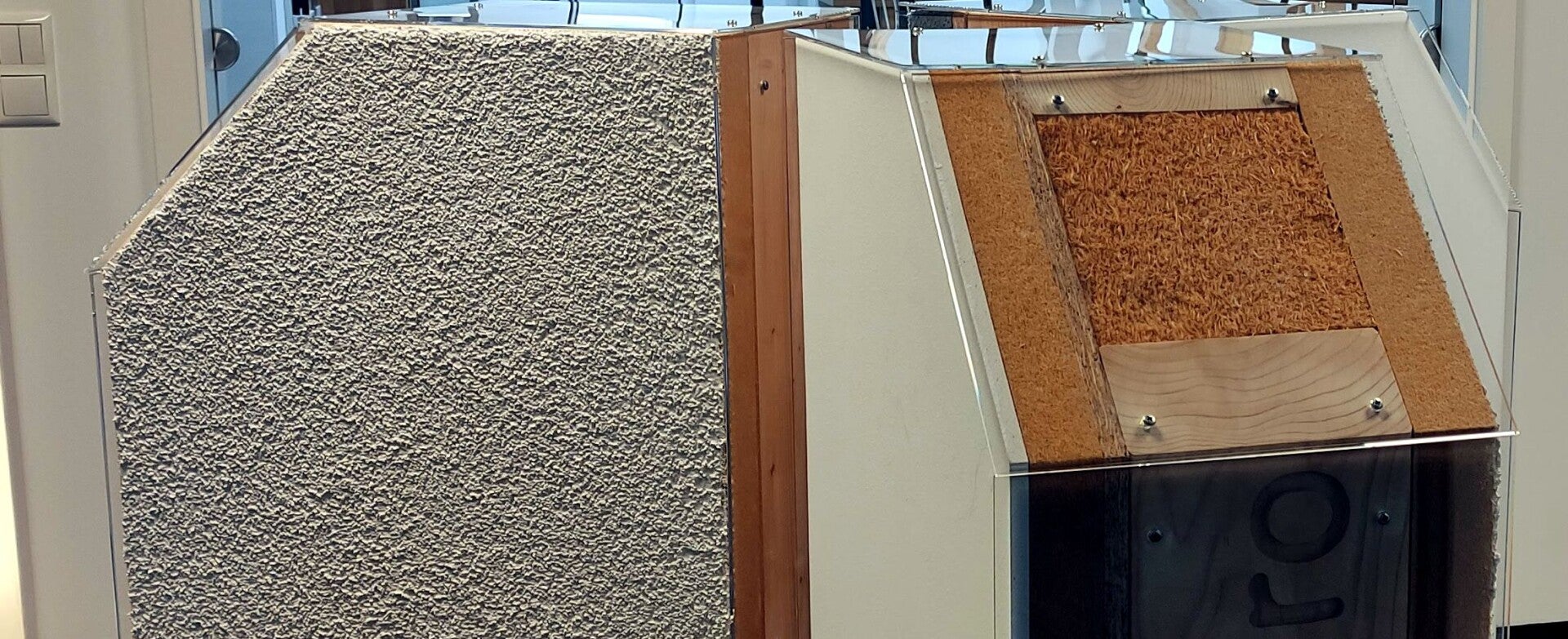 Die Montage eines modernen Fertighauses in Holzständerbauweise, bei der ein Kran ein werkseitig vorgefertigtes Wandelement inklusive bereits installierter Fenster zentimetergenau platziert