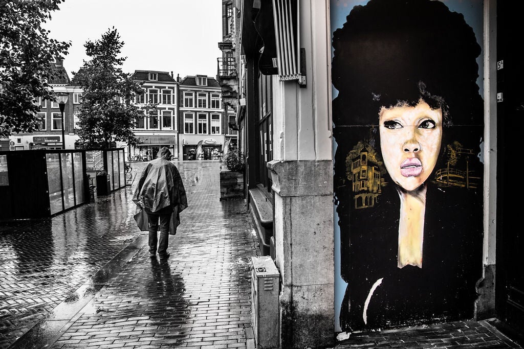 man rijd langs op step. Langs cafe de redding. Foto zwart wit. Street art kleur.