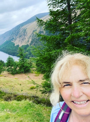 Tour Guide facing camera with beautiful scenery looking down on glendalough Upper Lake from a height