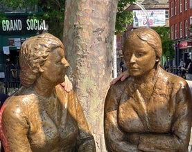 Close up of the bronze statue of two lady shoppers who are sitting on a bench and chatting