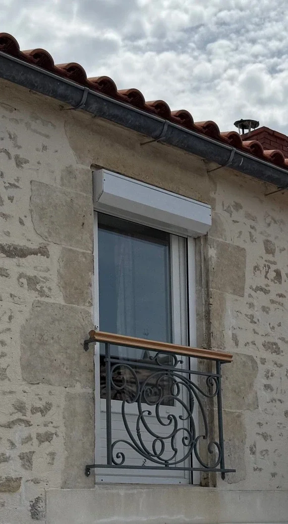 Garde-corps de fenêtre en fer forgé installé sur une façade en pierre d'une maison ancienne.