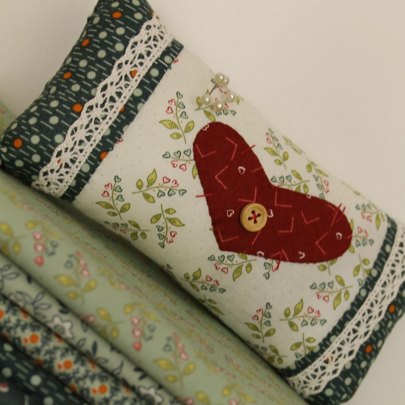 kussen op een stapel quiltstoffen op rol, in de kleuren groen en creme