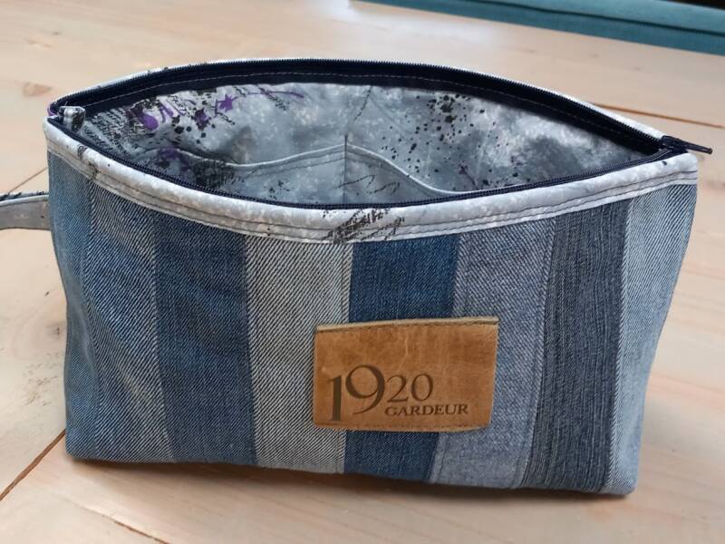 toilettassen van spijkerstof, met banen in verschillende kleuren blauw en een blauw randje naast de rits