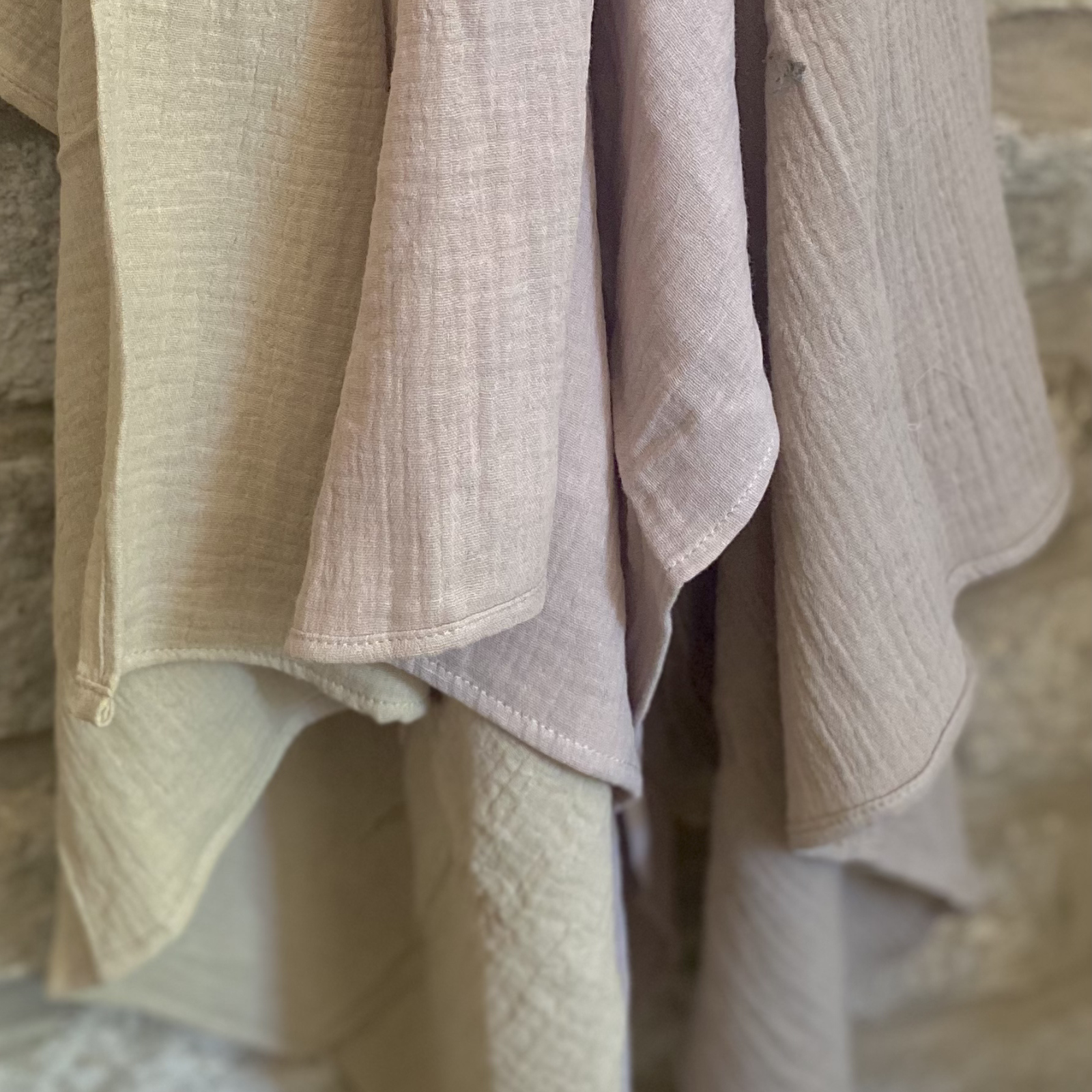 A cream organic cotton muslin cloth featuring a brown sun, moon, and stars pattern, elegantly draped over a rustic wooden stool, by The Little Soft Cloth.