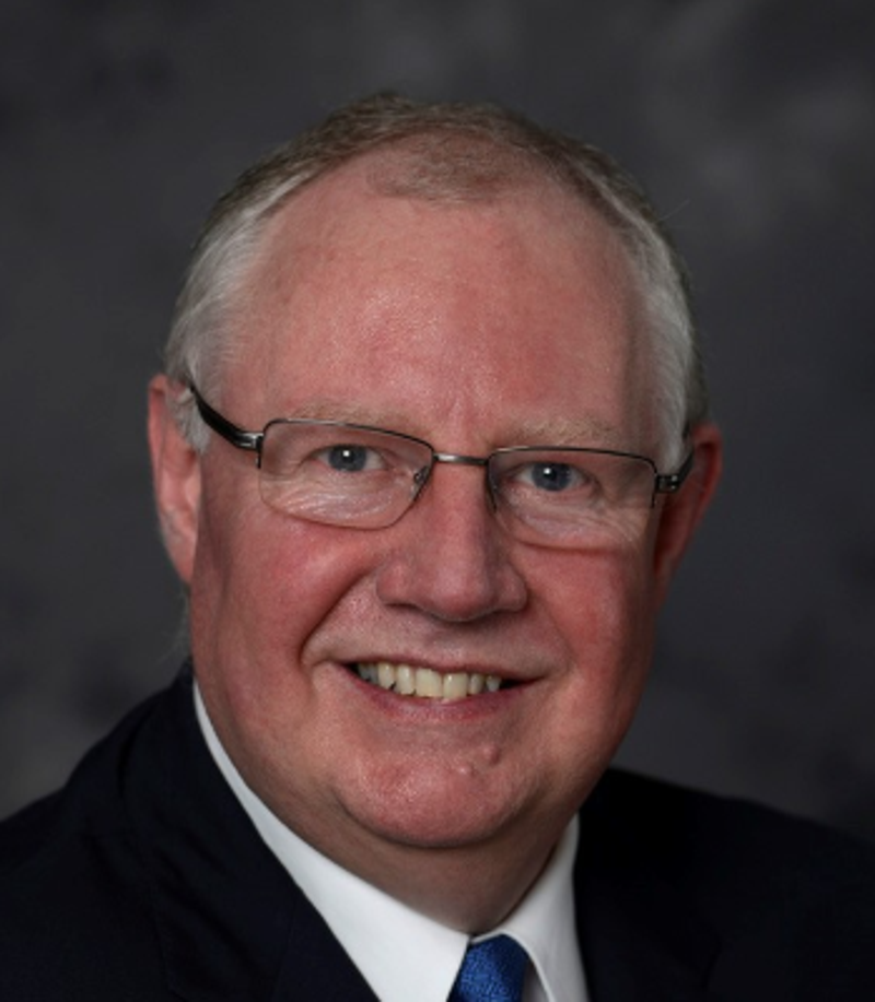 This image shows a smiling white man with glasses in a dark suit and blue tie. Leslie is committed to inclusive finance and accessibility.