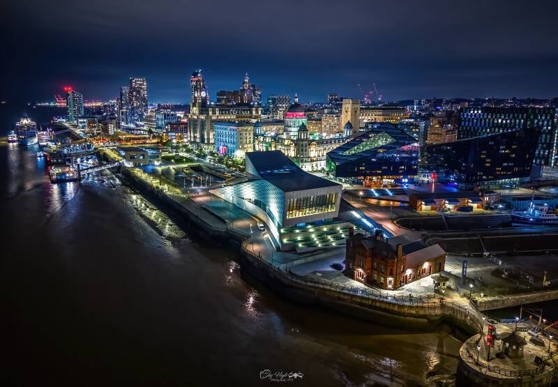 Aerial night view of Liverpool’s Pier Head, Museum of Liverpool and illuminated waterfront buildings beside the River Mersey, by Mike McMahon.