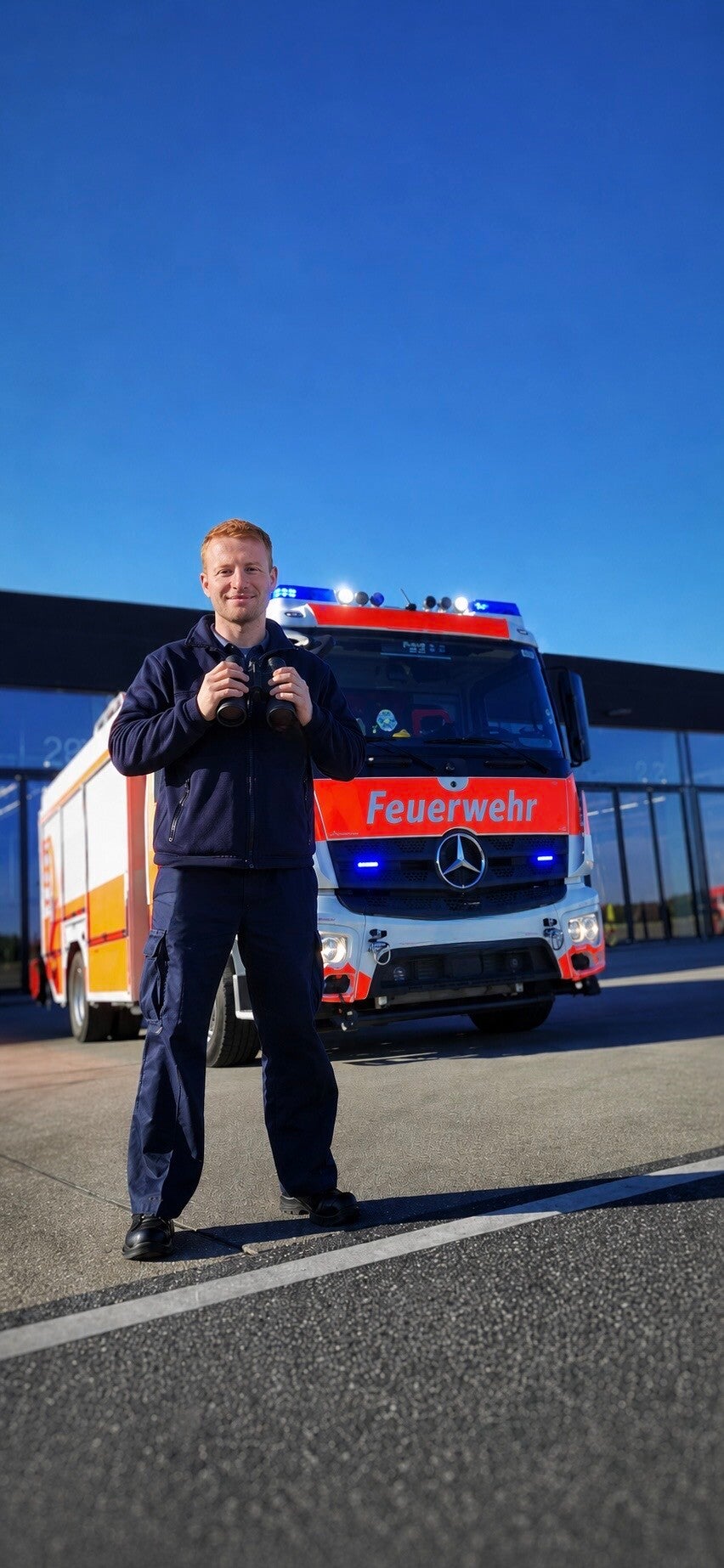 Im Hintergrund ein Feuerwehrauto, davor ein lächelnder Mann in Uniform