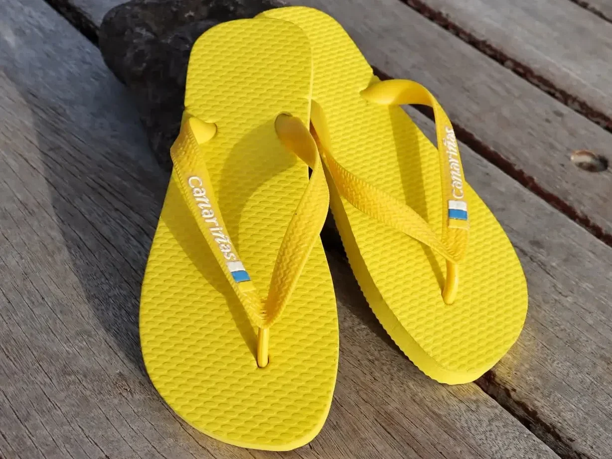 Chanclas Canariñas de color amarillo vibrante sobre madera rústica, calzado de verano con diseño de las Islas Canarias.