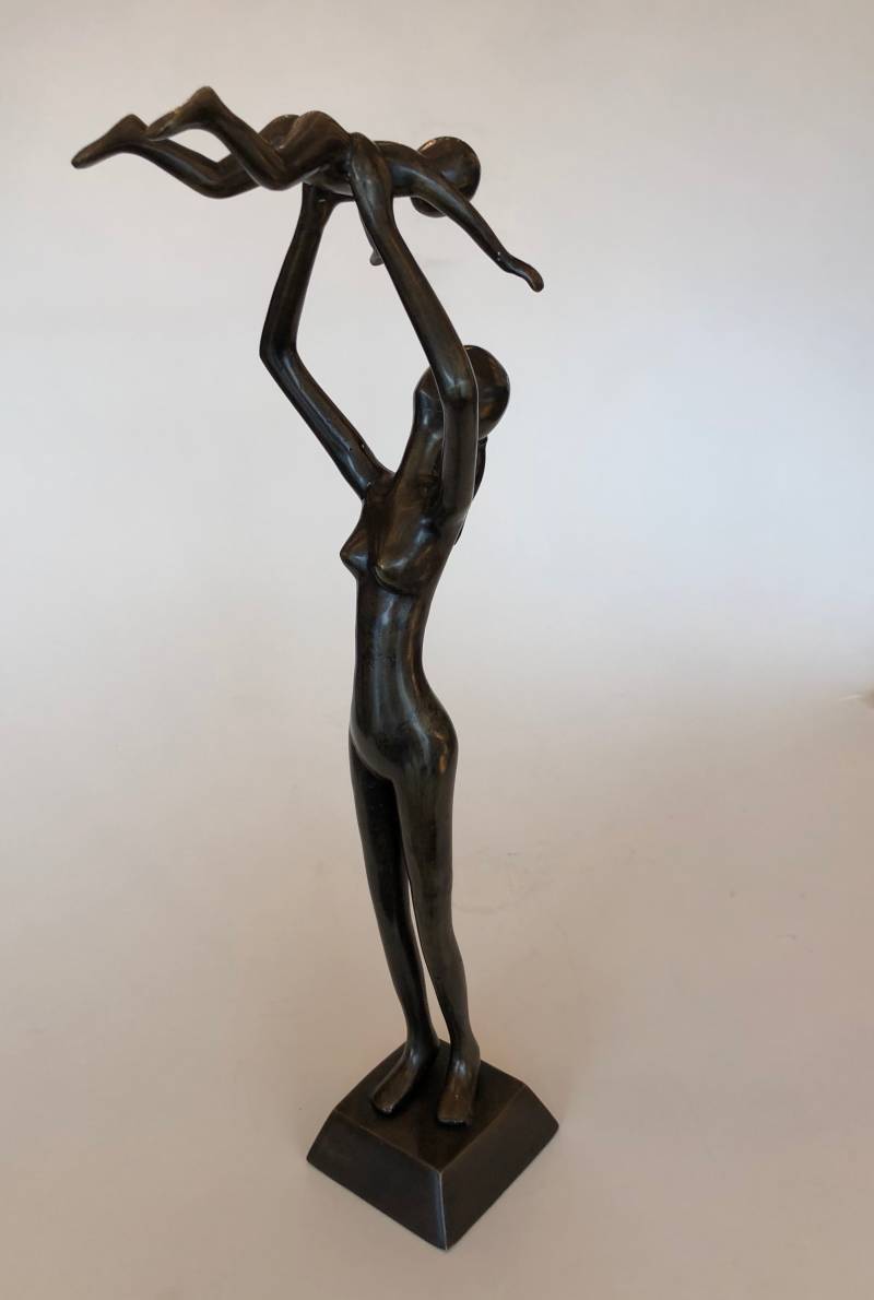 Staande moeder houdt kind omhoog in de lucht. Bronzen Beeld van beeldend kunstenaar Marius Verhagen.