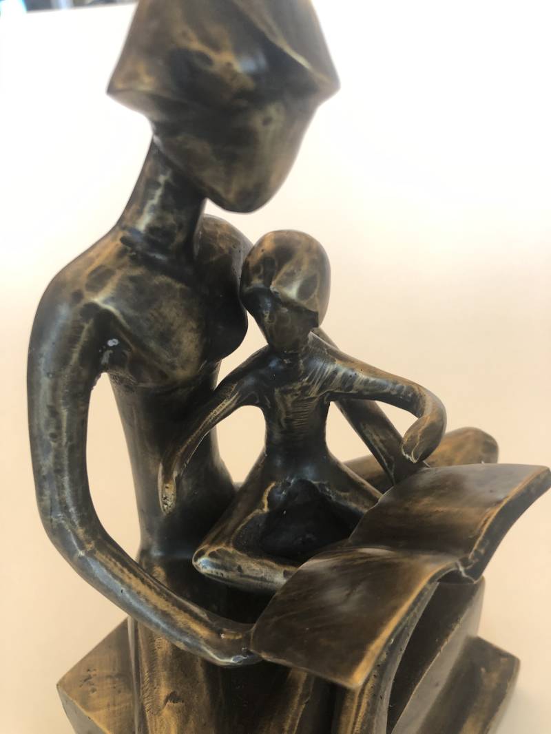 Moeder leest haar kind voor uit een boek op een sokkel in brons, licht abstract