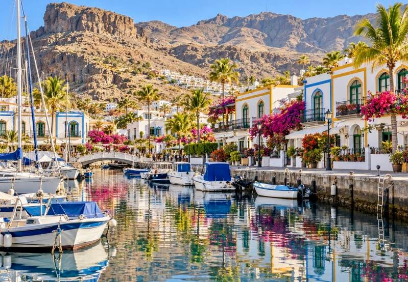Haven van Puerto de Mogán op Gran Canaria met boten, witte huizen en roze bougainvillea.