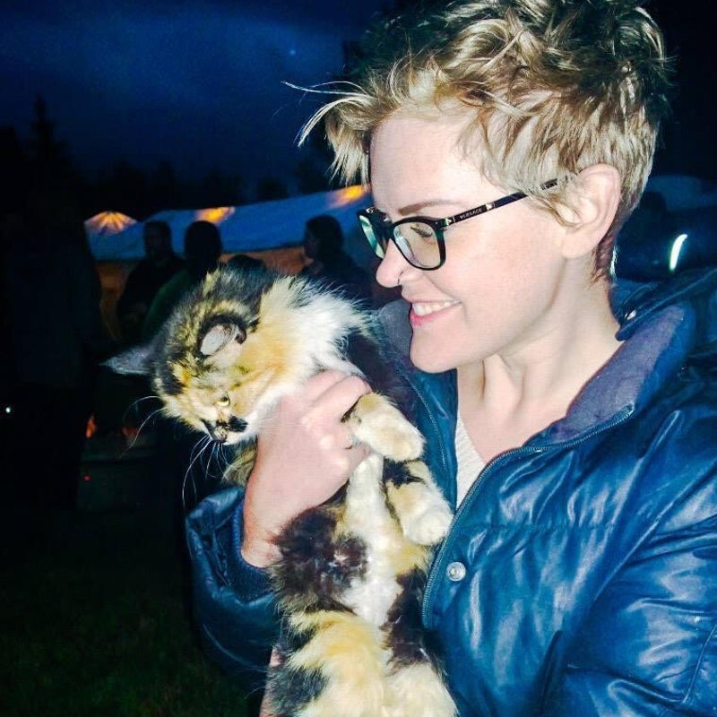 Woman with short hair holds a long-haired, calico cat who is looking away from the camera.