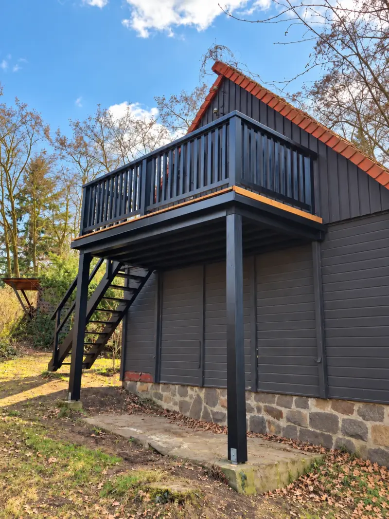 Neu gebauter Balkon mit dunkler Holzkonstruktion, Geländer und hellem Holzboden an einem Ferienhaus.