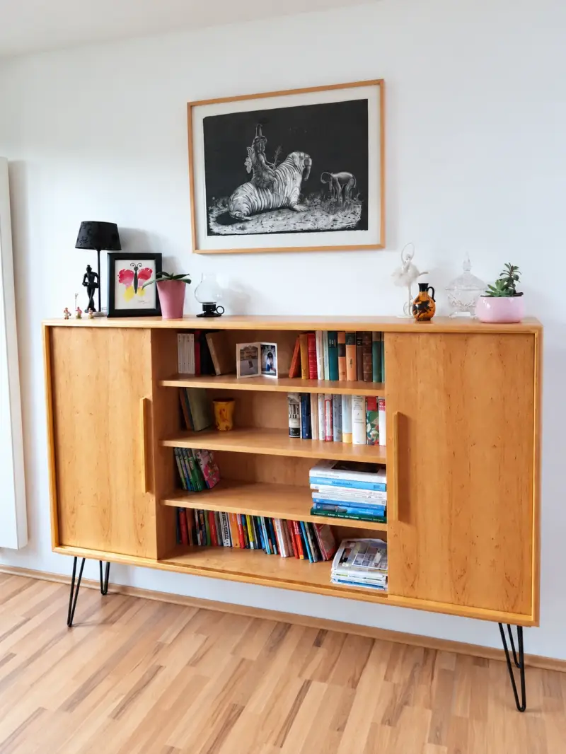 Maßgefertigtes Sideboard aus Erle mit Plattgoldrahmen, zwei Schiebetüren und filigranen Metallfüßen im Wohnraum.