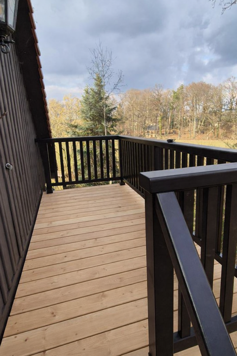 Neu gebauter Holzbalkon mit hellen Holzdielen und dunkel ausgeführtem Geländer an einem Ferienhaus.