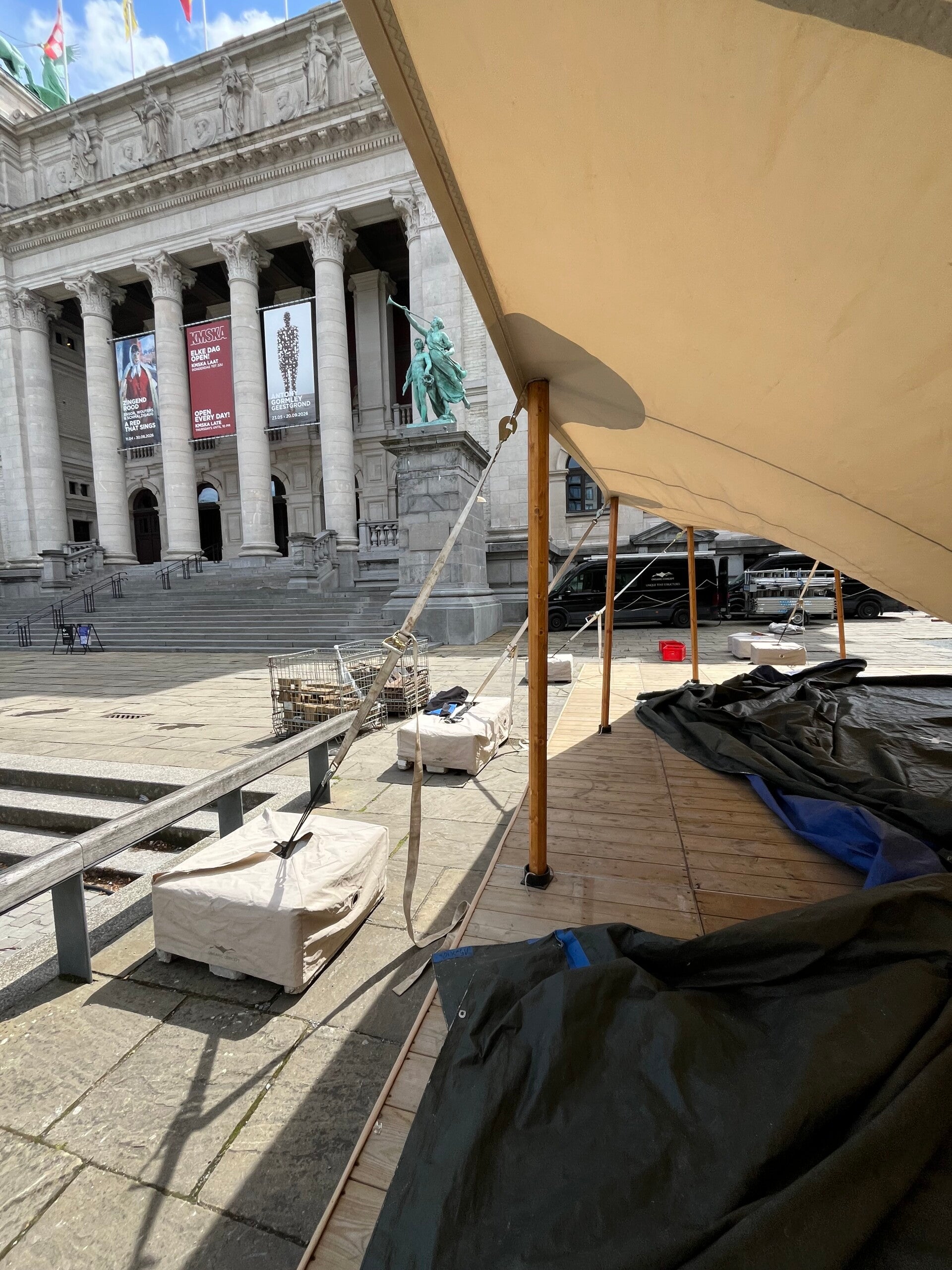 Detail van de silhouettetent opbouw in Antwerpen: houten palen, afspanning en museumgevel op de achtergrond.