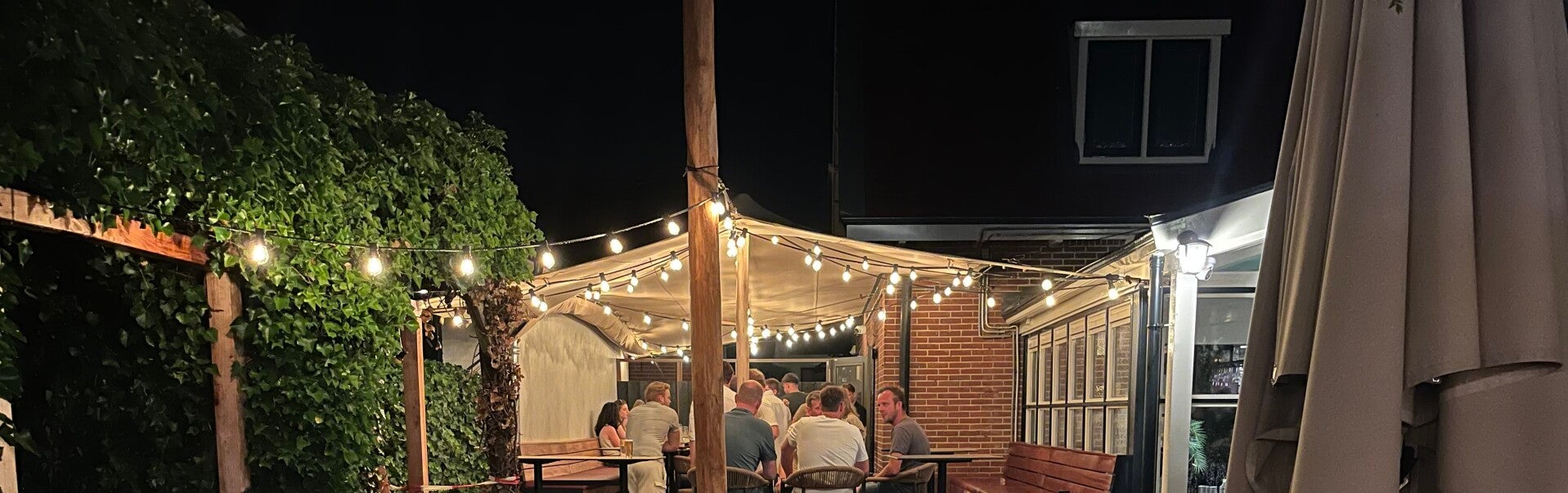 stretchtent op maat op terras tussen gebouwen met tafels en stoelen eronder