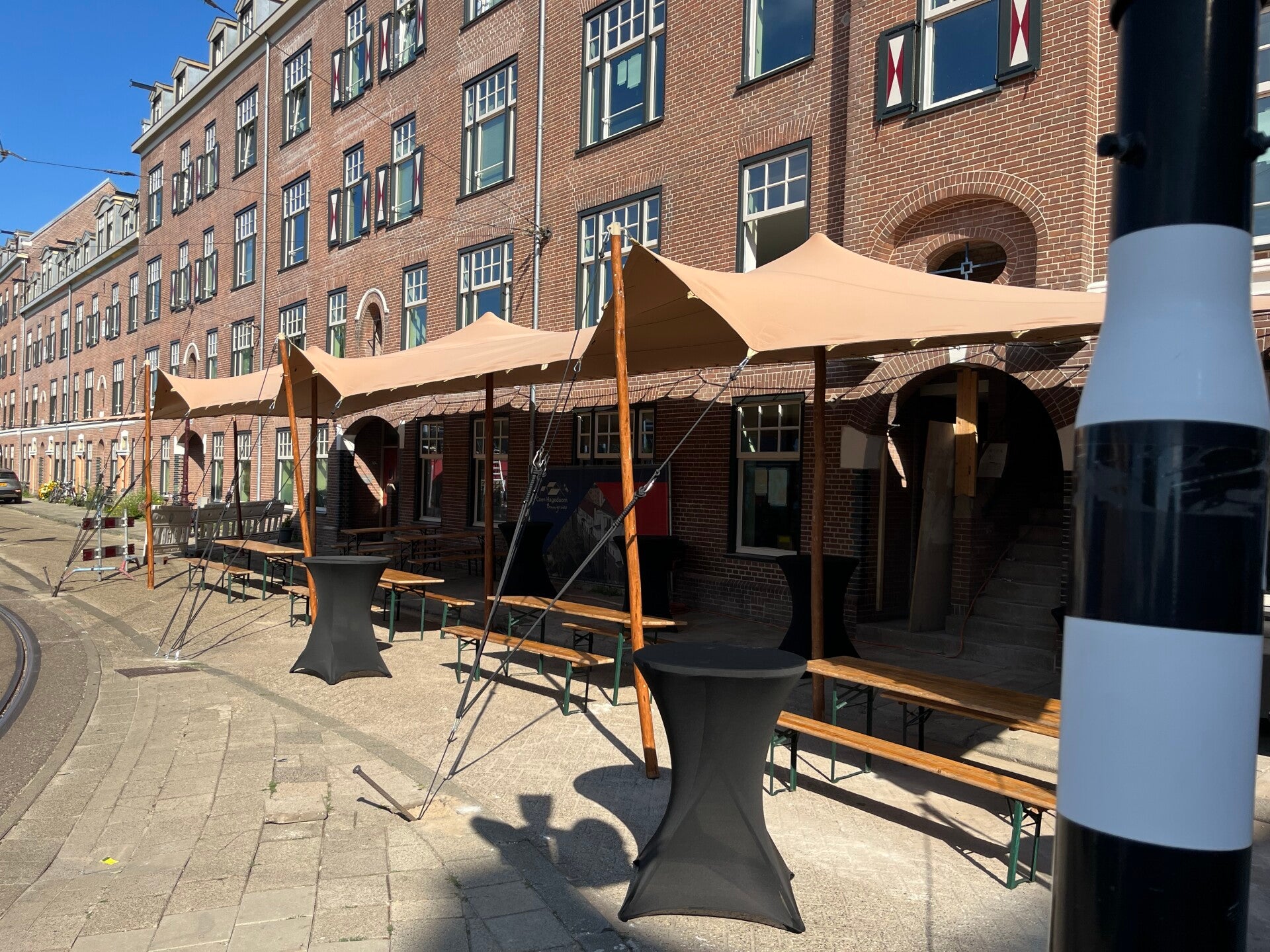 Stretchtent naast een paddelbaan bij een tennisclub vereniging, met terras eronder, flextent heeft houten palen en zandkleurig tentdoek