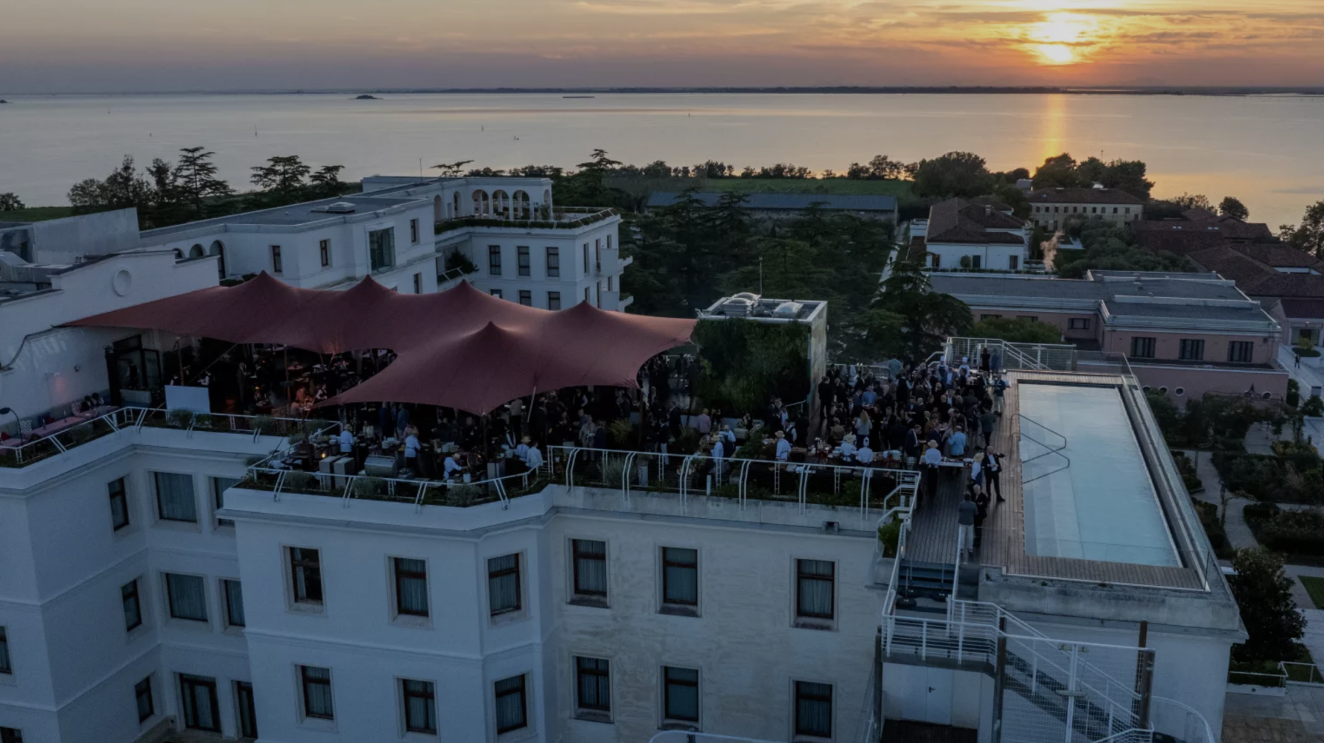 Bordeauxrode stretchtenten op een dakterras tijdens een evenement met uitzicht over het water bij zonsondergang