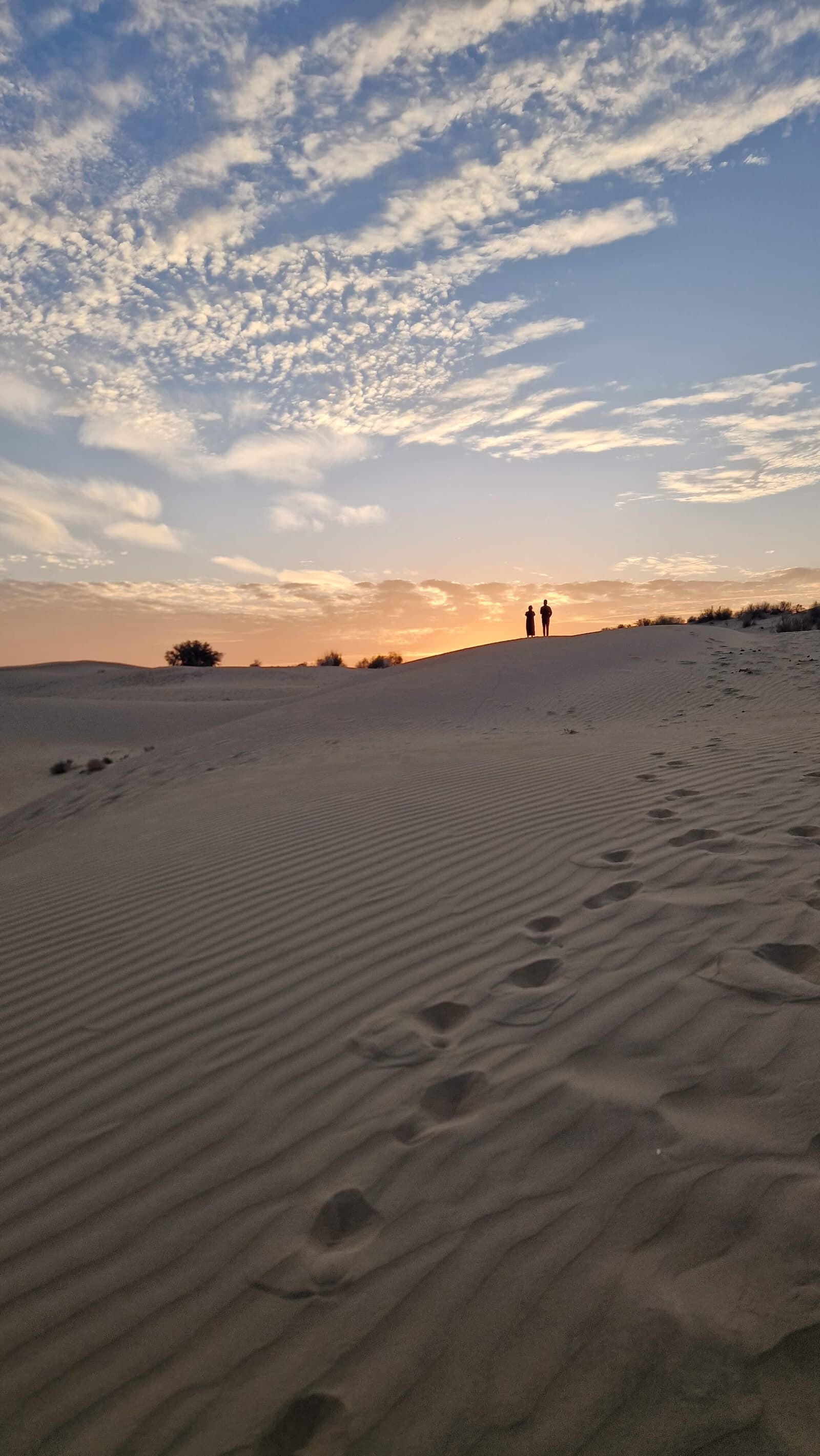 two people in the distance looking at a desert sunrise with footprints in the sand, symbolising options and possibilities