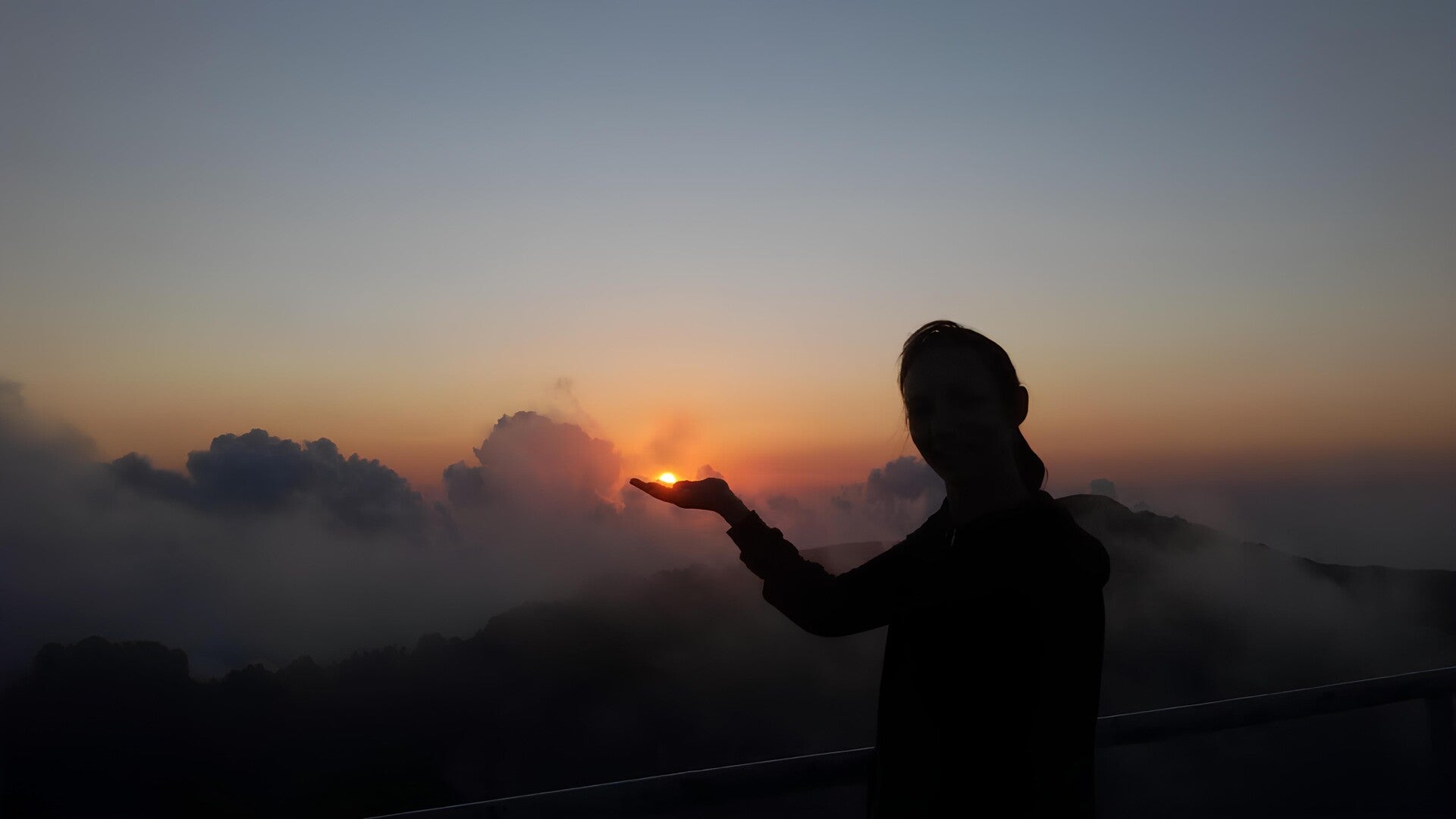Sunrise with clouds and mist, with the silhouette of a person appearing to hold the rising sun, symbolising personal healing and the quiet power of working in silence and solitude