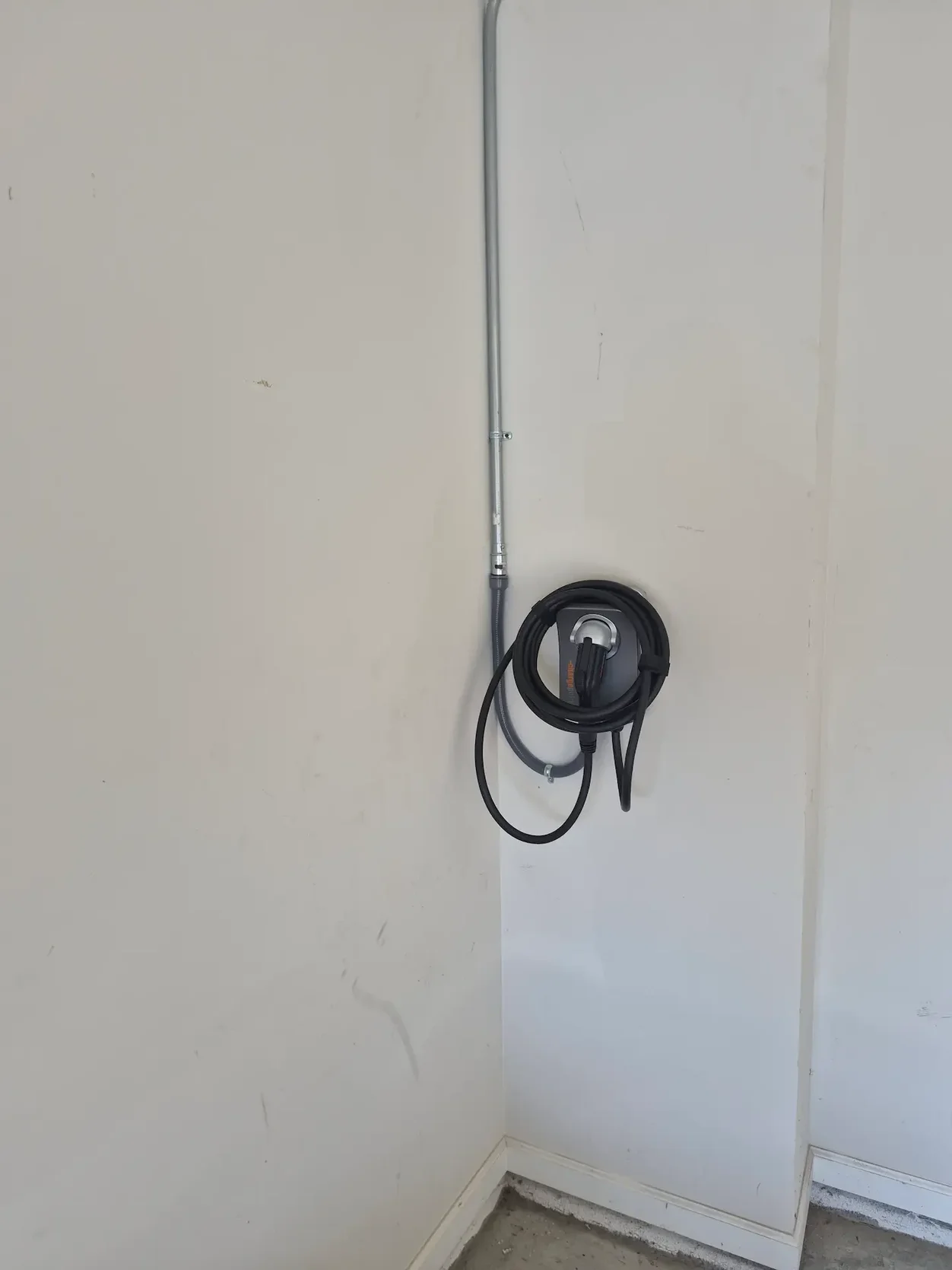 Completed ChargePoint Level 2 charger installation with conduit entering from above and the cable stored on the wall