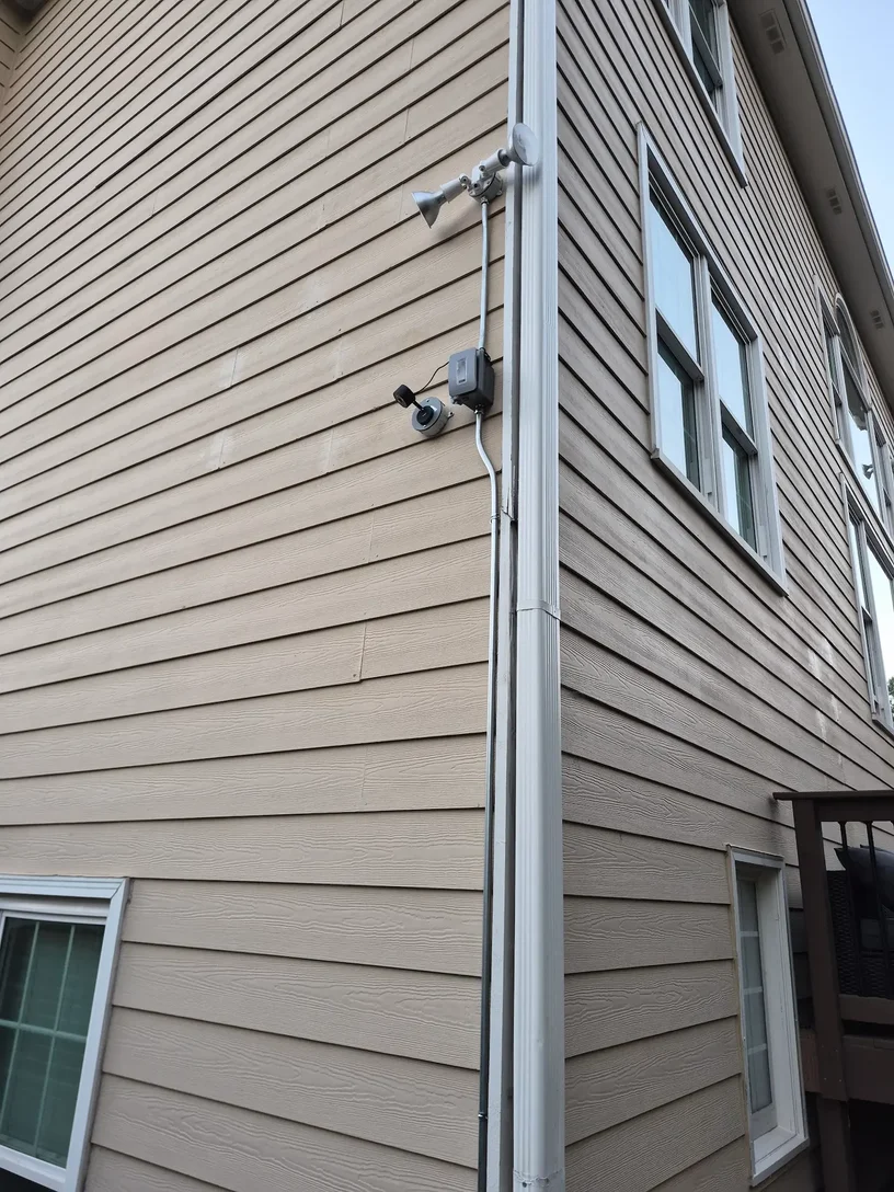 Outdoor security camera, floodlights and surface-mounted conduit installed along the side of an Alpharetta Georgia home