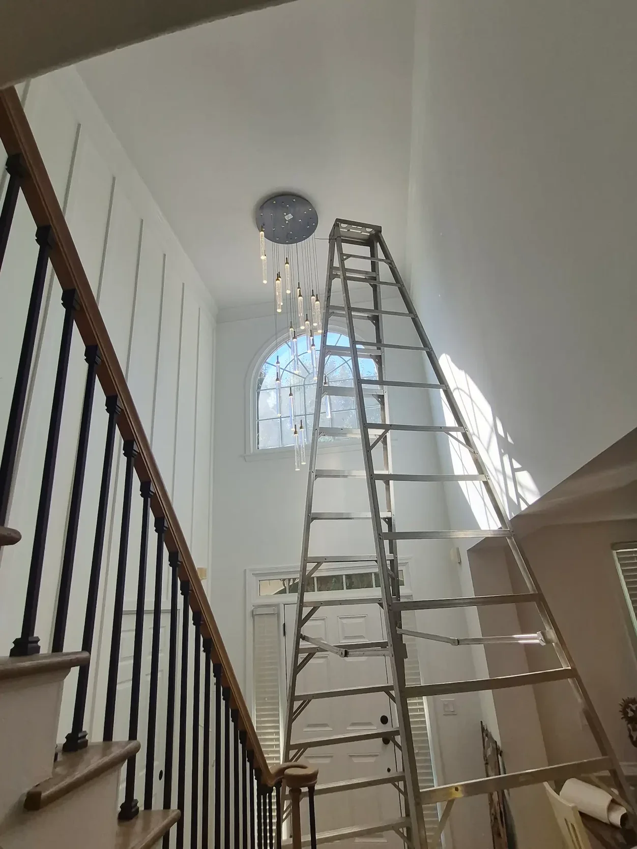 Modern cascading LED chandelier being installed in a high-ceiling Alpharetta Georgia entryway