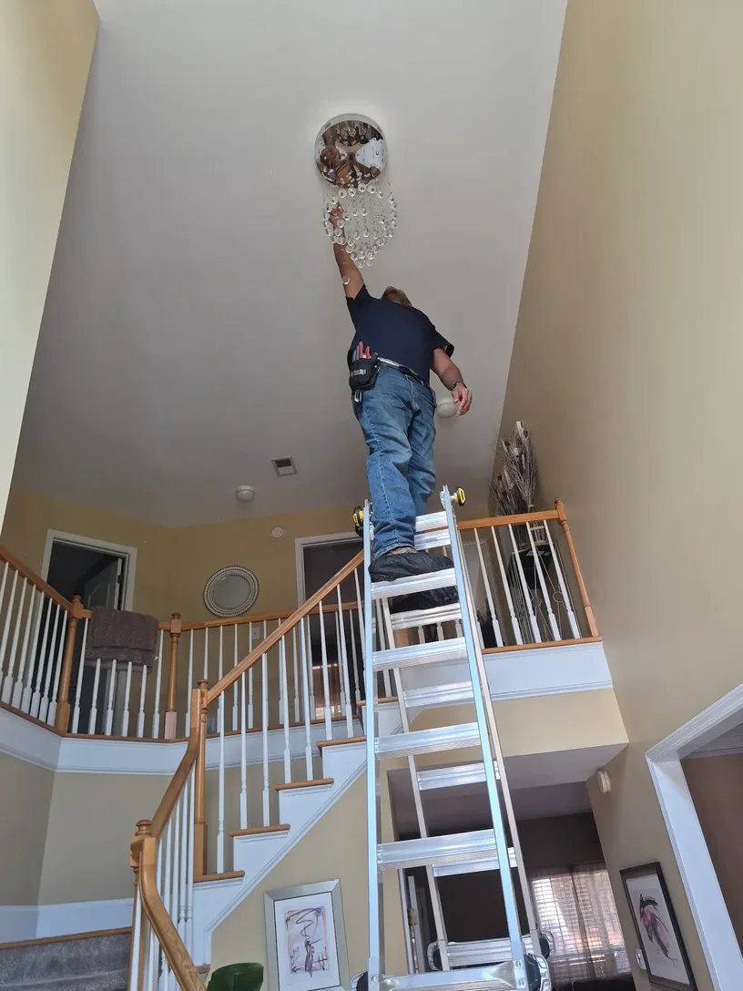Technician on a tall ladder installing a crystal chandelier at an 18 foot entryway ceiling