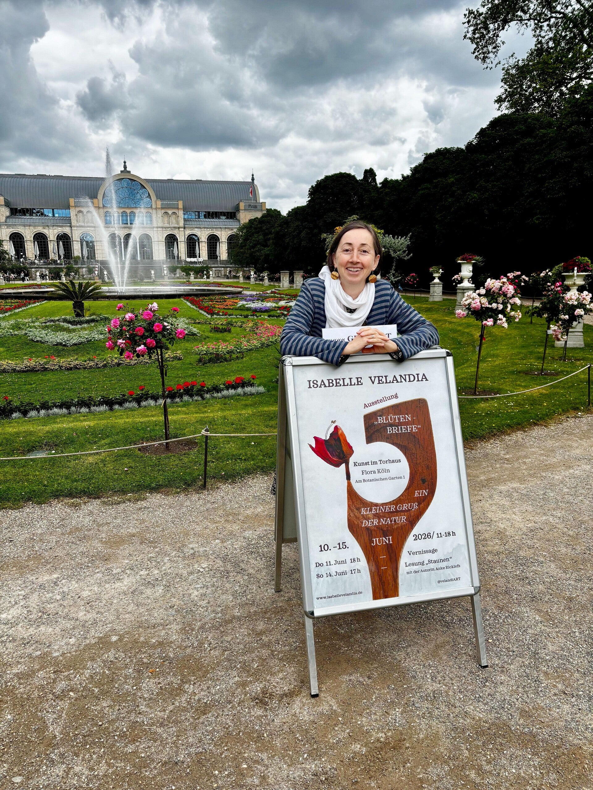 Ein Portrait der Künstlerin Isabelle Valandia vor der schönen Kulisse der Flora Köln mit Springbrunnen
