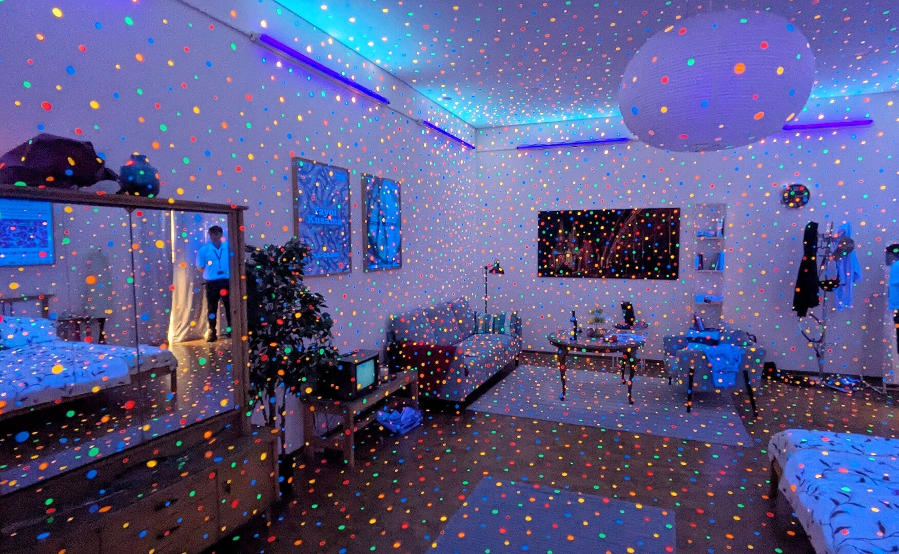 Ein ganzer Raum mit Bett, Sofa und Schrank im vollen UV Licht und vielen bunten Punkten  bei der Ausstellung  Yayoi Kusama im Museum Ludwig in Köln