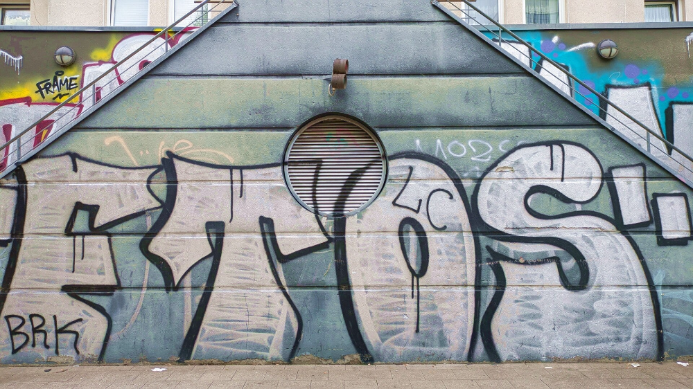 Grauer Schriftzug als StreetArt auf einer Wand – Köln-Mülheim