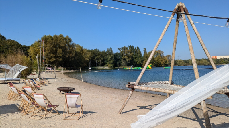 Blick auf gemütliche Liegestühle im feinen Sand des Blackfoot Beach am Fühlinger See, umgeben von einer entspannten Strandatmosphäre.