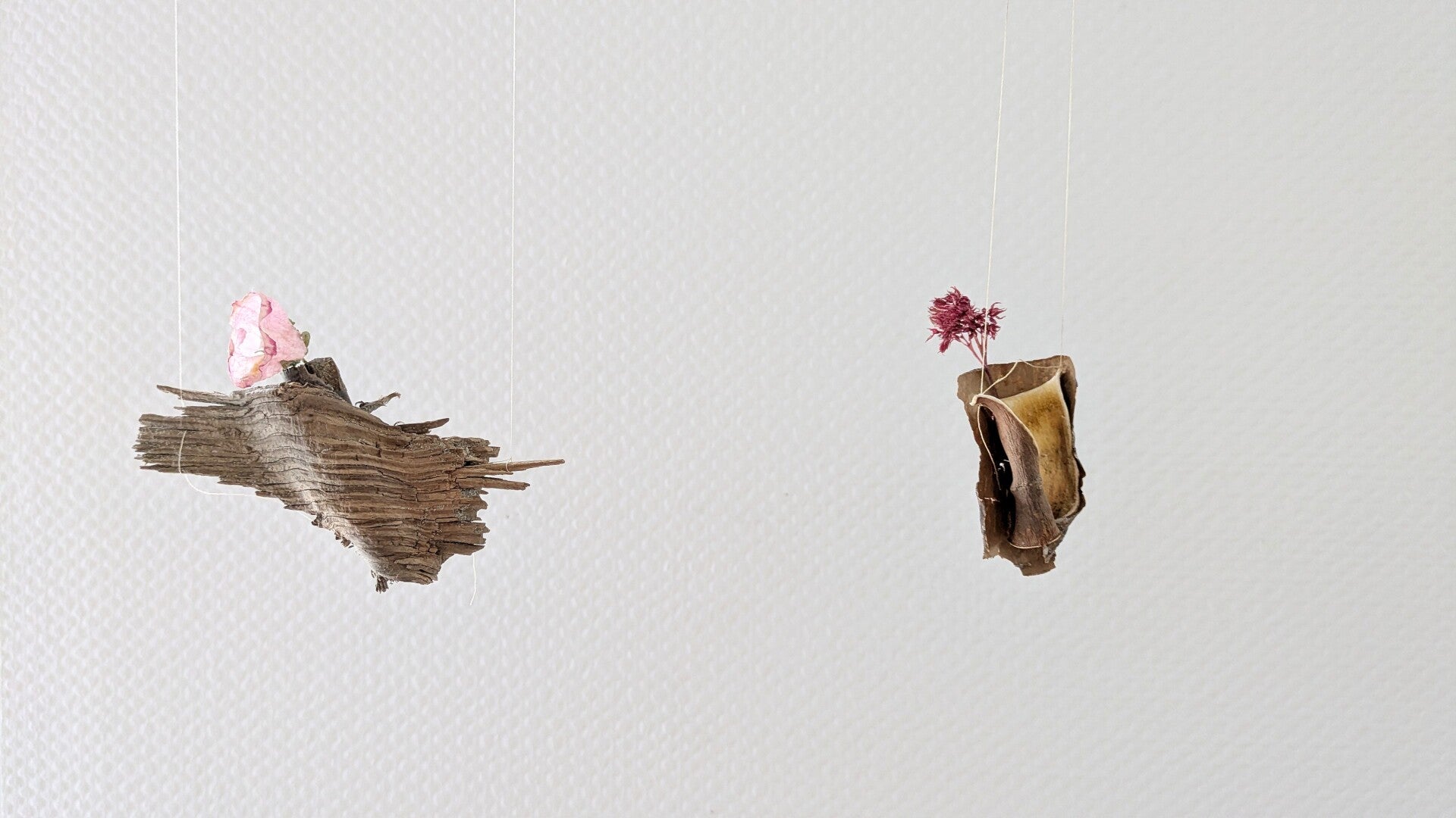 Zwei filigrane schwebende Objekte aus Rinde mit einer kleinen Blüte verziert in der Ausstellung „Blütenbriefe“.