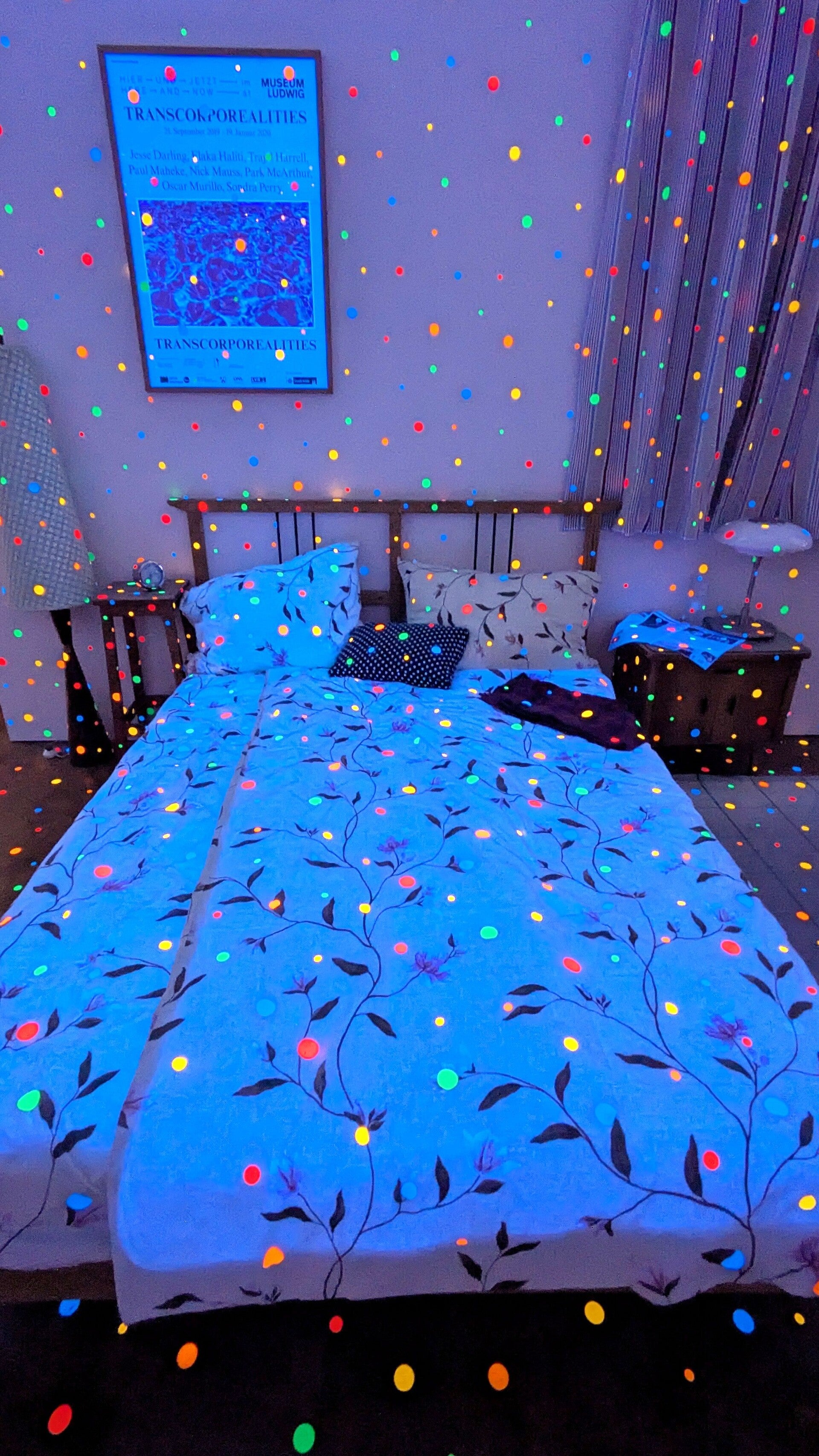 Ein Blick auf ein Bett in einem Zimmer mit vielen bunten Punkten im UV Licht  bei der Ausstellung  Yayoi Kusama im Museum Ludwig in Köln