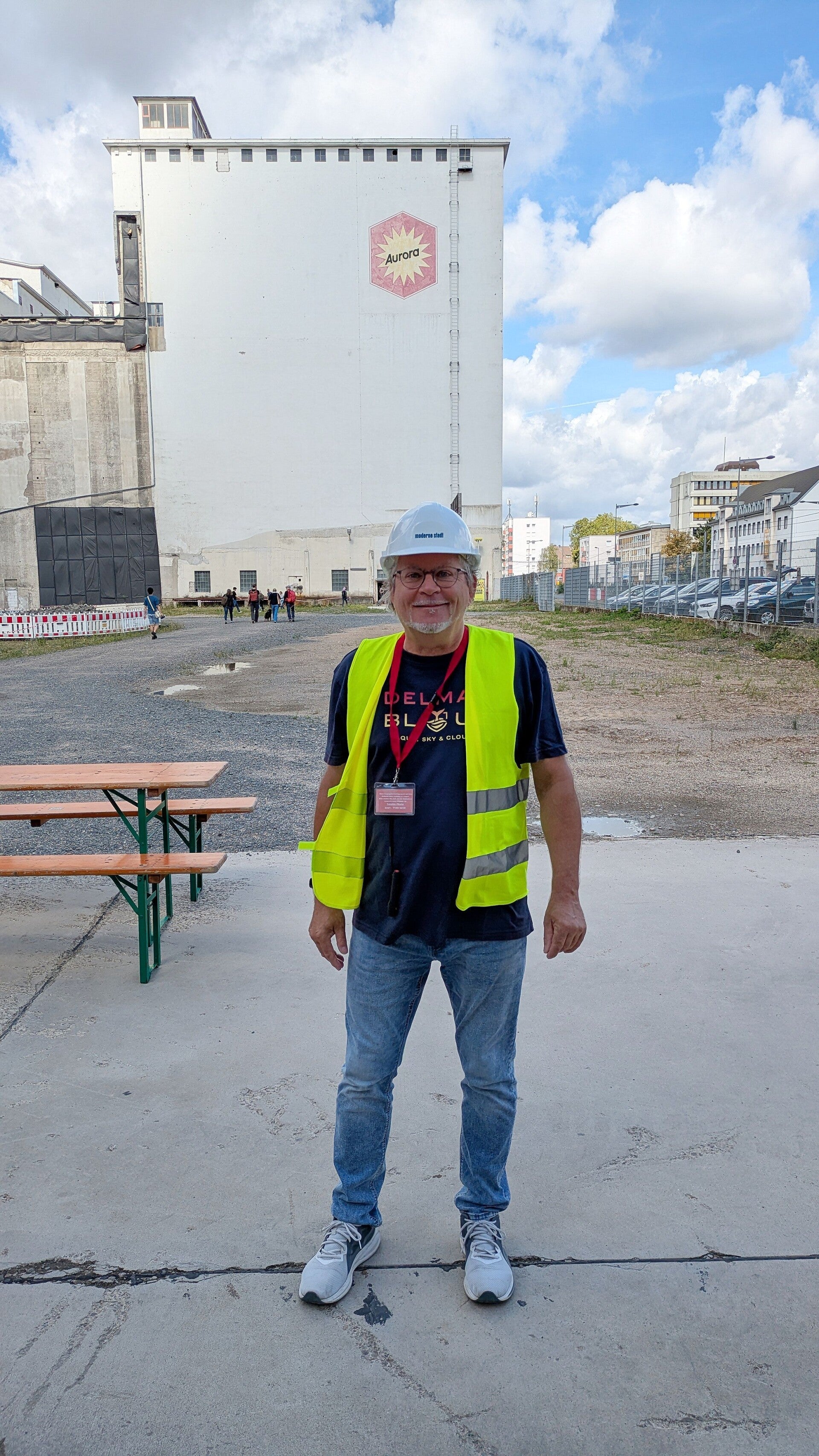 Ein Foto von mir selbst, mit einem Schutzhelm, einer Warnweste  und einem Besucherausweis vor dem Gebäude Aurora Mühle in Köln Deutz