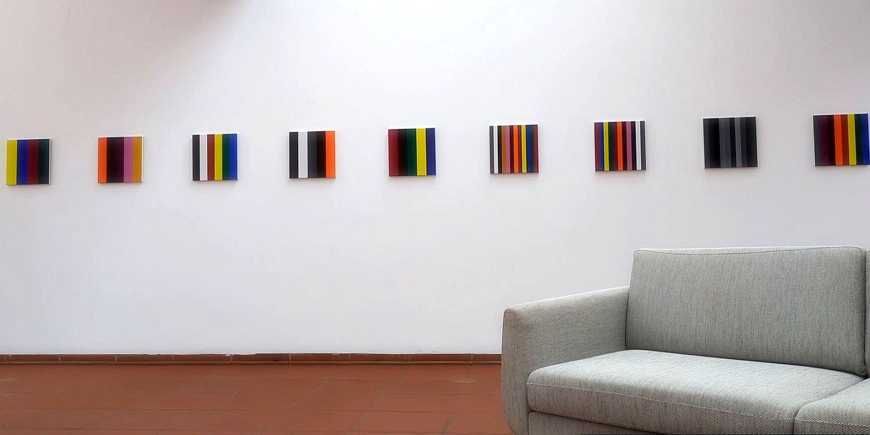 Mehrere kleine farbige Kunstwerke an der Wand über einem gemütlichen Sofa