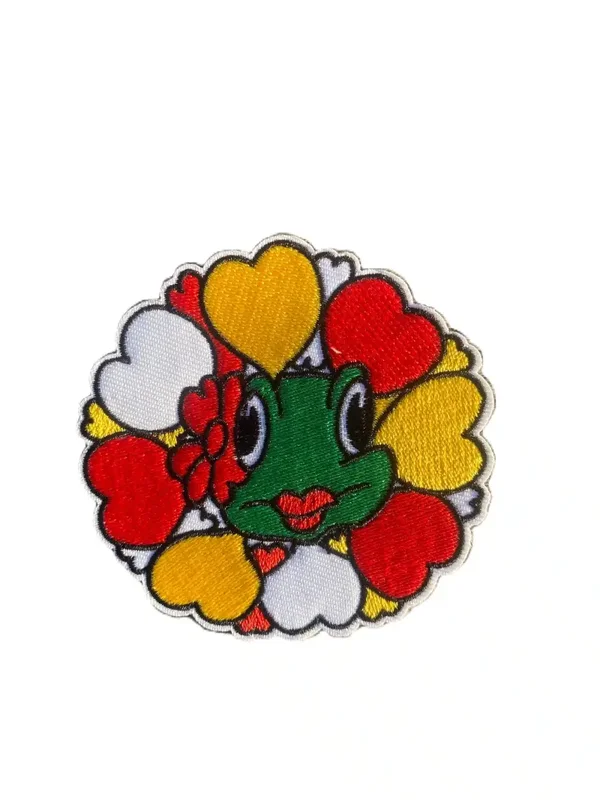 Embleem: rondje met hartjes middenin kikker met bloem