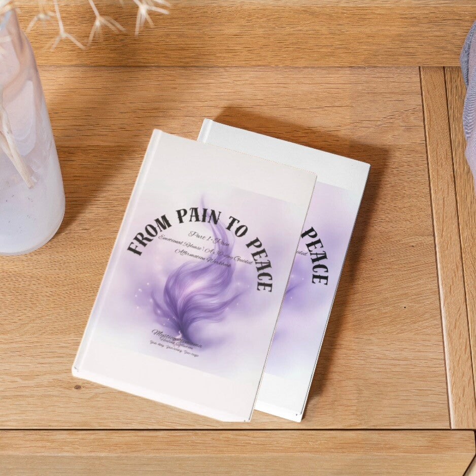 self-help journal, "FROM PAIN TO PEACE," with a white translucent cover and a soft, glowing purple smoke or feather graphic, photographed on a natural wooden surface indoors.