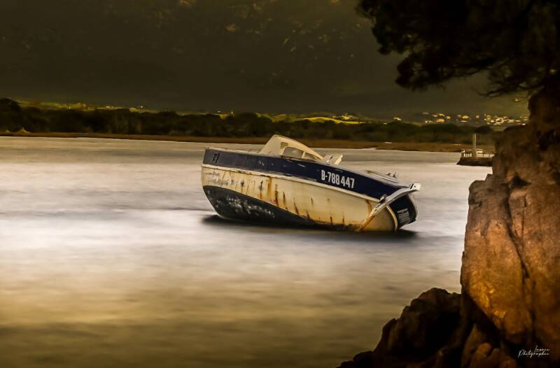 Bateau abandonné au crépuscule, flottant immobile dans une eau dorée sous un ciel sombre, ambiance atmosphérique