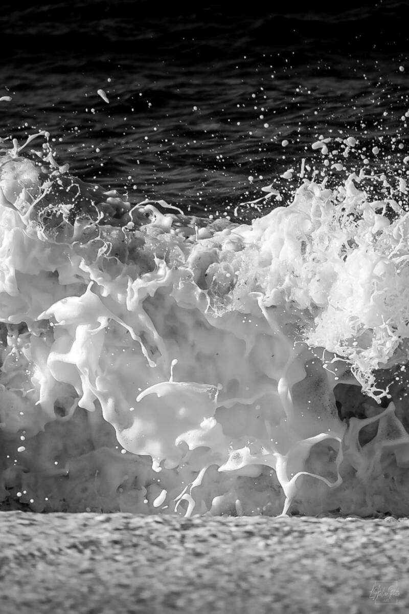 Gros plan d’écume éclatant en gerbes blanches sur fond de mer sombre.