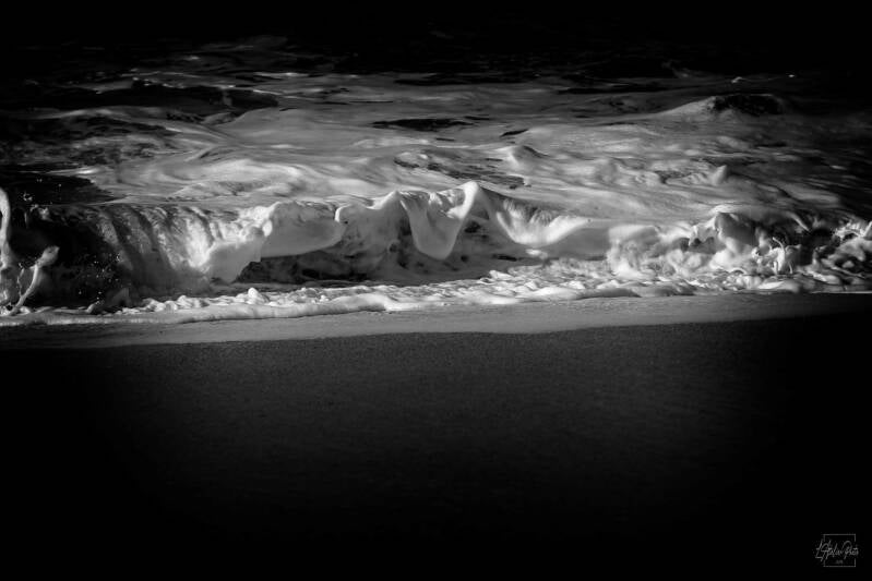 Vague douce et sombre se retirant sur le sable, écume blanche en avant-plan