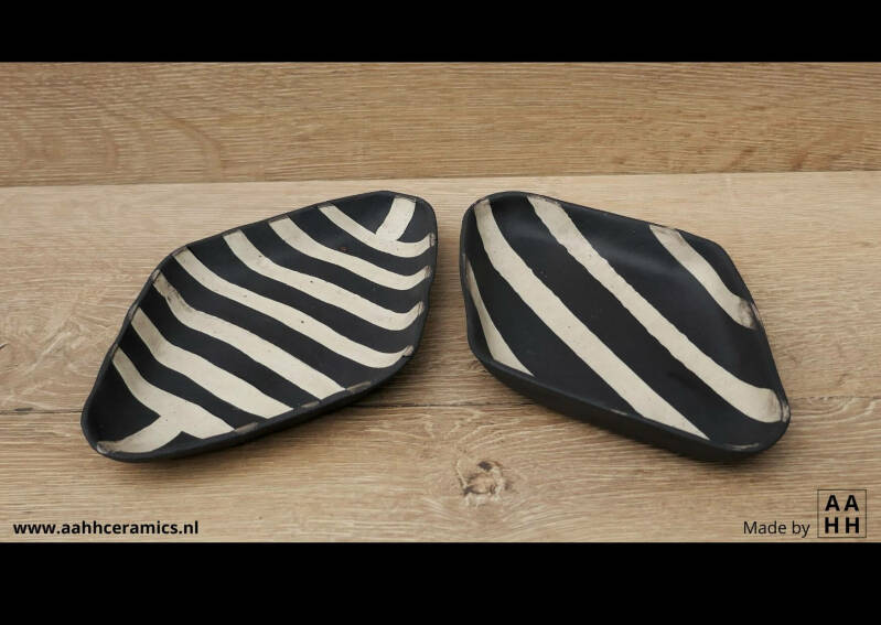 2 ruitvormige schaaltjes van zwarte klei met daarin witte kleirolletjes gerold.